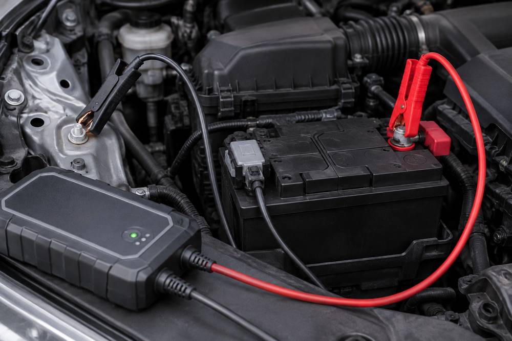Chargeur branché sous le capot : pince rouge sur la borne positive de la batterie, pince noire sur un goujon de masse de la carrosserie, capteur gris sur la borne négative
